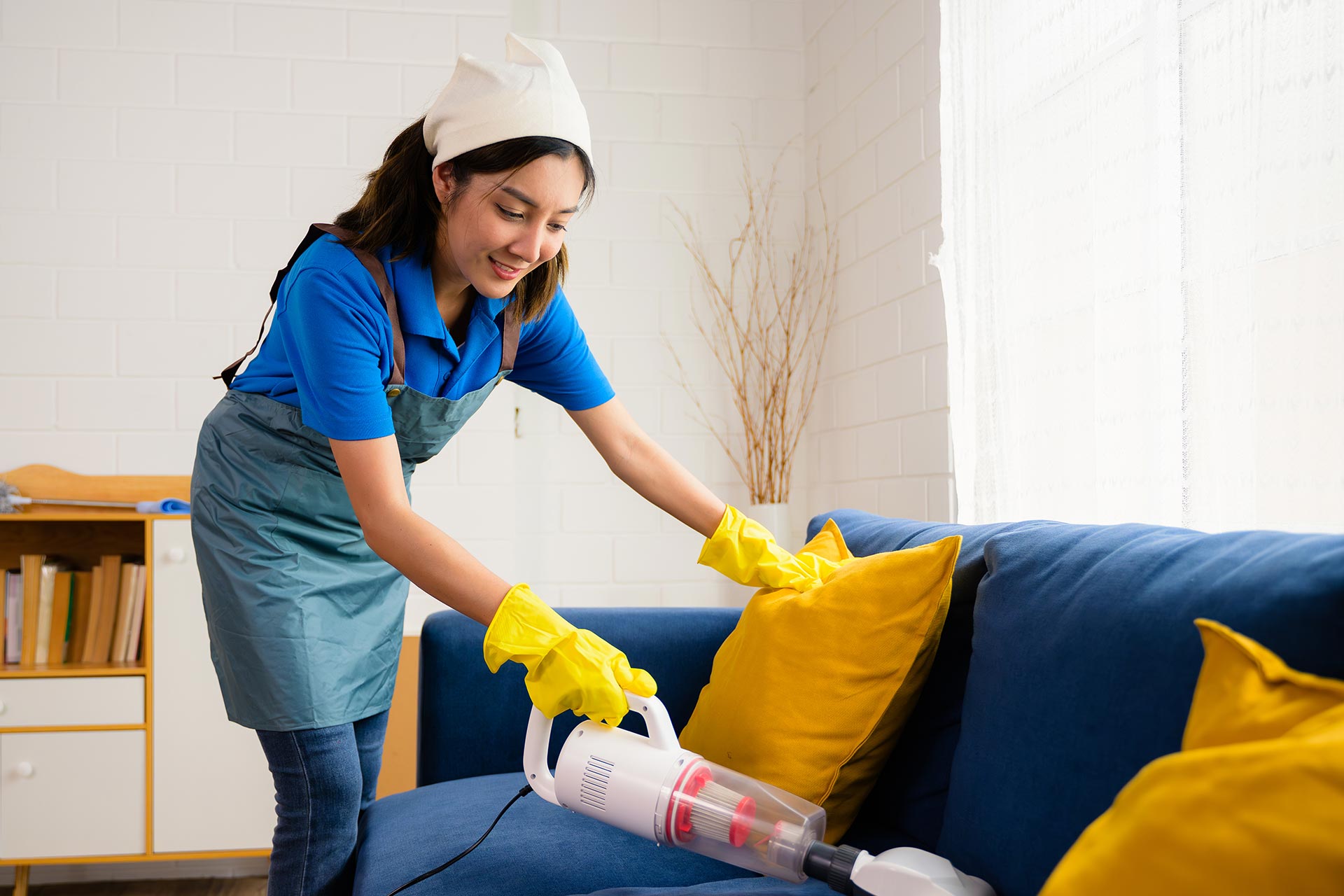 A cleaning service lady cleaning the sofa with vacuum cleaner.